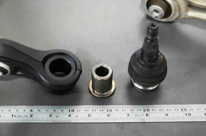 Automotive parts including a control arm, CV joint, and bearing on a gray surface with a ruler for scale.